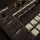 Detailní pohled na ovládací panel černého elektronického nástroje značky Roland. Jsou vidět posuvníky s popisky 1, 2, 3, 4 a FX PRM, FX DEPTH, VOLUME…
