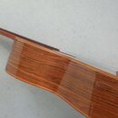Detailní pohled na zadní část korpusu a hmatník akustické kytary. Nástroj má hnědý lakovaný povrch s viditnou strukturou dřeva. Na fotce nejsou žádné…