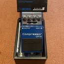 Modrý efekt pedál značky BOSS v originální krabici. Na pedálu jsou nápisy Compressor, CP-1X a čtyři ovládací prvky s popisky LEVEL, ATTACK, RATIO a C…