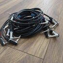 Svršek dřevěné podlahy, na které leží několik černých audio kabelů s konektory typu jack. Některé kabely mají červené označení u konců. Na povrchu je…