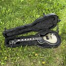 Elektrická kytara s tónem sunburst v černém tvrdém kufru. Na hlavě hředu je viditelné logo Epiphone. Kytara má tmavý hmatník s bílými vložkami a dvě…