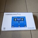 Bílá krabice s modrým vokálním procesorem. Na krabici je nápis VOICELIVE play a pod ním text 3-Button Vocal Effects Stompbox with Looping, v pravém d…