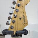 Zadní strana hlavy kytary z přírodního dřeva s chromovanými ladičkami. Na dřevě je černý nápis Fender® a STRATOCASTER®, v horní části je drobným písm…