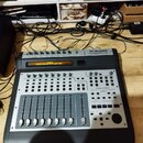Černý kontrolér s kovovým horním panelem. V pravém horním rohu je nápis M-AUDIO PROJECTMIX I/O. Displej zobrazuje text M-Audio Control Surface is in…