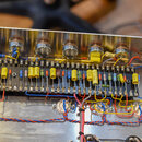 Fotografie zachycuje vnitřní pohled do elektronického zařízení s kovovým šasi. Je vidět řada elektronických součástek, včetně kondenzátorů v žlutých…