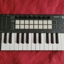 Černý kompaktní MIDI kontrolér s klaviaturní klávesnicí a 16 bílými čtvercovými pady. Na horním panelu je nápis LAUNCHKEY MINI a řada ovládacích knof…