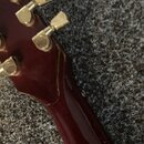 Detail zadní strany hlavy a krku červené kytary. Na ladících kolenkách je viditelný nápis GIBSON. V místě spoje hlavy a krku je viditelná prasklina v…