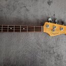 Fotografie zobrazuje hridel a krk elektrické basové kytary s dřevěným povrchem. Na hlavě je viditelné logo Fender a nápis JAZZ BASS®, pod ním je menš…