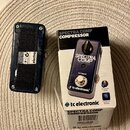 Kytarový efekt v tmavě modré barvě a jeho původní kartonové balení. Na krabici i na efektu je nápis SPECTRA COMP COMPRESSOR a logo tc electronic. Na…