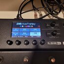 Černý kytarový procesor značky LINE 6 POD. Na displeji je vybraný preset s názvem 29B Ace Frehley a jsou vidět další názvy presetů: 29A REVV Solo, 29…