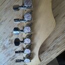 Detail hlavy kytary z přírodního dřeva s šesti chromovanými ladičkami. Na každém ladičku je bílý kulatý štítek s nápisem Professional Guyker Tuning m…