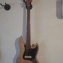 Elektrická basová kytara s přírodním dřevěným povrchem těla a hředu. Nástroj má černý pickguard, dva snímače a čtyři ladicí kolíky na hlavě. Na těle…