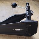 Černý pedál k basové bubnu s kovovou konstrukcí a protiskluzovou gumovou ploškou. Na mechanismu je vidět nastavovací šroub a řetězové tahlo. Povrch v…