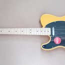 Žlutá elektrická kytara s černým pickguardem a světlým hnedým hřednicí. Na hlavě je nápis TELECASTER Squier. Na pickguardu je nalepená červená kulatá…