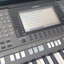Digitální klavír značky YAMAHA, model PSR-S370. Na displeji je zobrazen text s názvem „Blues, Katapult“ a následnými sloky v češtině. Nástroj je v do…