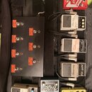 Černý pedalboard v přepravním kufru s řadou efektů. Na levé straně je černý spínací box s červenými štítky s nápisy: CH 1 DIRTY, CH 1 CLEAN, CH 2 MOD…