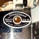 Detail ovalného štítku na bubnu s nápisem Slingerland. Štítek obsahuje text QUALITY DRUMS, NILES, ILLINOIS U.S.A. a SER. NO. 32280. Povrch štítku i o…
