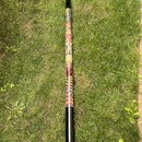 Didgeridoo s černým povrchem na koncích a barevným ornamentálním vzorem v prostřední části. Vzor obsahuje červené, žluté a bílé prvky s motivemi zvíř…