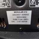 Detailní záběr na zadní stranu černého elektronického zařízení s bílou nálepkou. Na nálepce je uveden text: MODULAR 212, 220/240V~ 50/60HZ, 300VA MAX…
