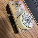 Kytarový efekt s černým šasi a horním panelem z materiálu s texturou dřeva. Na panelu je umístěn stomeč a bílé otočné kolečko s nápisy TONE WHEEL GUI…