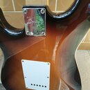 Zadní strana elektrické kytary s lakem v přechodu od žluté přes hnědou k černé barvě. Na kovové spojce krku a těla je vyryto logo Squier. V dolní čás…