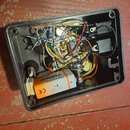 Fotografie zachycuje vnitřek černého plastového šasi efekt pedálu s odkrytými elektronickými součástmi a zapojením kabelů. Uvnitř je umístěna baterie…
