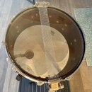 Fotografie zachycuje pohled zshora na buben s průhlednou blánou. Na bláně je vidět logo REMO a nápis REMO CLEAR HEAD MADE IN U.S.A. Přes buben je nat…