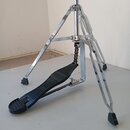 Fotografie zobrazuje chromovaný stojan s integrovaným pedálem, pravděpodobně pro činely. Pedál je vyroben z černého plastu s žebrovaným povrchem a je…