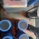 Detailní pohled do vnitřku elektronického zařízení s kovým šasi. Na stříbrném kovovém krytu je fialový nápis DE T4145-A. V dolní části jsou vidět čty…
