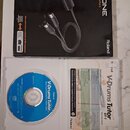 Fotografie zobrazuje krabici s USB MIDI rozhraním Roland UM-ONE a otevřený plastový obal s CD diskem a příručkou. Na krabici je nápis UM-ONE USB MIDI…