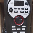 Černý elektronický modul s bílým vnějšími rámem, umístěný v kartonové krabici. Na zařízení jsou nápisy Roland, DRUM SOUND MODULE TD-11 a V-Drums. Mod…