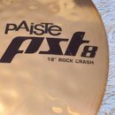 Detailní pohled na mosazný činel s kovaným povrchem. Na povrchu je černý nápis pAiste, pod ním stylizovaný model pst8 a označení 18" ROCK CRASH. Povr…