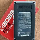 Fotografie zachycuje zadní stranu efekt pedálu značky BOSS v kovovém šasi. Na spodní části je štítek s tabulkou BOSS AC ADAPTOR, nápisem Dry battery…