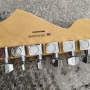 Zadní strana dřevěné hlavy kytary s šesti chromovanými ladičkami. Na dřevě je černý nápis MADE IN MEXICO a SERIAL NUMBER MX20169490. Na ladičkách jso…