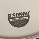 Detail bílého bubnového koženě s černým potiskem. Je na něm vidět logo SONOR a nápisy White Medium, DRUM HEAD, MADE BY REMO a U. S. A. Povrch je hlad…