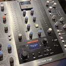 Stříbrno-černý studiový procesor značky Solid State Logic. Na panelu jsou četné otočné knoflíky, tlačítka a digitální displej s nápisem STATUS Awaiti…