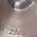 Detailní záběr na povrch kovového činely v stříbrné barvě s koncentrickými rýhami. Na povrchu je vyryto logo Zildjian. Nástroj vykazuje běžné známky…