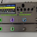 Stříbrný kytarový procesor s kovovým povrchem a digitálním displejem. Na horním pravém rohu je nápis GE300 a pod ním text Guitar Multi-Effects Proces…