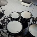 Elektronická bicí souprava v černé barvě s bílými membránami. Na bubnech jsou viditelná loga Roland a nápisy V-Drums. Souprava obsahuje čtyři pady bu…