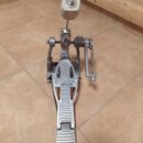 Stříbrný kovový basový pedál s bílým beaterem. Na základní desce je viditelný nápis TAMA IRON COBRA. Povrch vykazuje známky běžného používání a mírné…