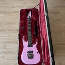 Růžová elektrická kytara v tvrdém kufru s červeným polstrováním. Na hlavě hmatníku je bílý nápis Ibanez. Kytara má dva humbuckery, Tremolo most a čer…
