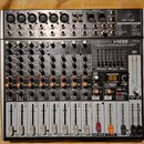 Stříbro-šedý mixážní pult značky behringer s nápisem XENYX X1222USB. Zařízení obsahuje 6 mikrofonních vstupů, několik linkových vstupů a faderové ovl…