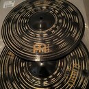 Dvě černé činely s koncentrickými zlatavými rýhami. Na horním číneli je viditelné logo "m" a nápis "METAL". Na spodním číneli je zobrazen nápis "META…