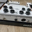 Bílý efekt pedál s černými ovládacími knoflíky a kovovými spínači. Na horní straně je logo ve tvaru stylizovaného písmena „G“ a nápis FKT AUDIO. Na b…