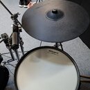 Fotografie zachycuje část elektronické bicí soupravy. Je vidět černý činel a bílý buben, oba s logem Roland. Na bubnu je dále nápis V-Drums a pod ním…