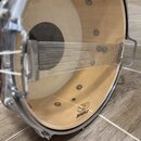 Detailní pohled do vnitřku snare bubnu s kovovým rámem a světle hnědým dřevěným korpusem. Na spodní straně korpusu je černý nápis SONOR a vedle něj t…