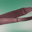 Hnědý kožený popruh na hudební nástroj. Na povrchu je vyražen nápis SOLOSTRAP a vedle něj stylizovaný nápis Nes. Popruh je vybaven řadou otvorů pro n…