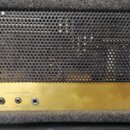 Zadní strana kytarového komba s černou perforovanou kovovou mřížkou a zlatým spodním panelem. Na panelu jsou nápisy EFFECT, LOUDSPEAKER OUTPUTS a ozn…