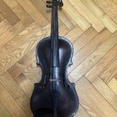 Tmavě hnědá smyčcová viola z dřeva s lakovaným povrchem. Nástroj je zobrazen v celku z pohledu zepředu a leží na dřevěné podlaze. Na fotce nejsou žád…