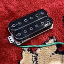 Černý humbucker s dvěma řadami magnetů a viditelnými póly. Na pravém okraji je bílý nápis XH 2. Snímač má kovové rámečky a z něj vede zelený kabel. P…